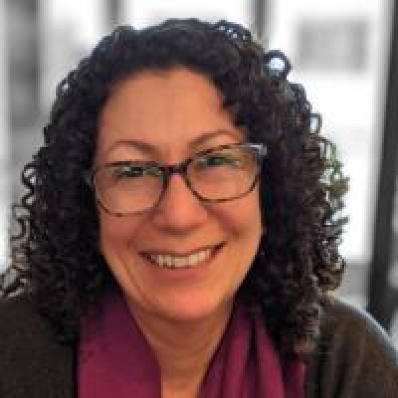 Jennifer Mahdavi smiling wearing glasses, and a magenta scarf and a brown sweater.